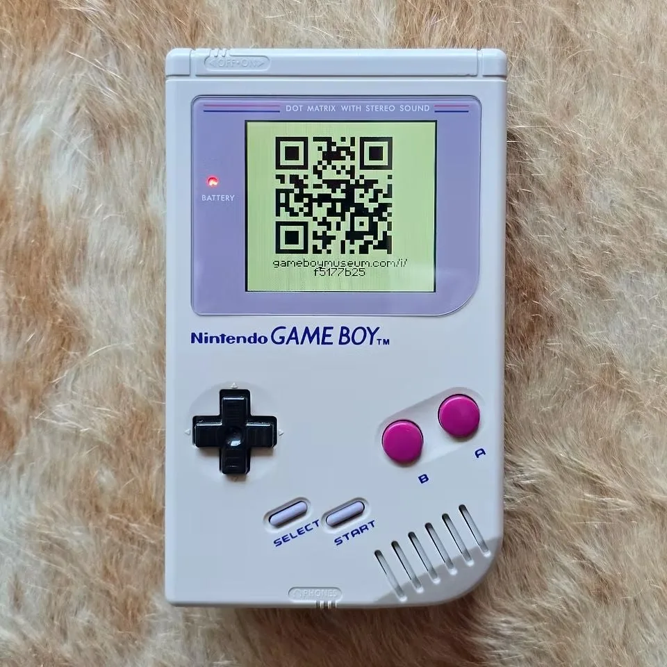 Fehér Game Boy konzol, a kijelzőn egy QR-kóddal.